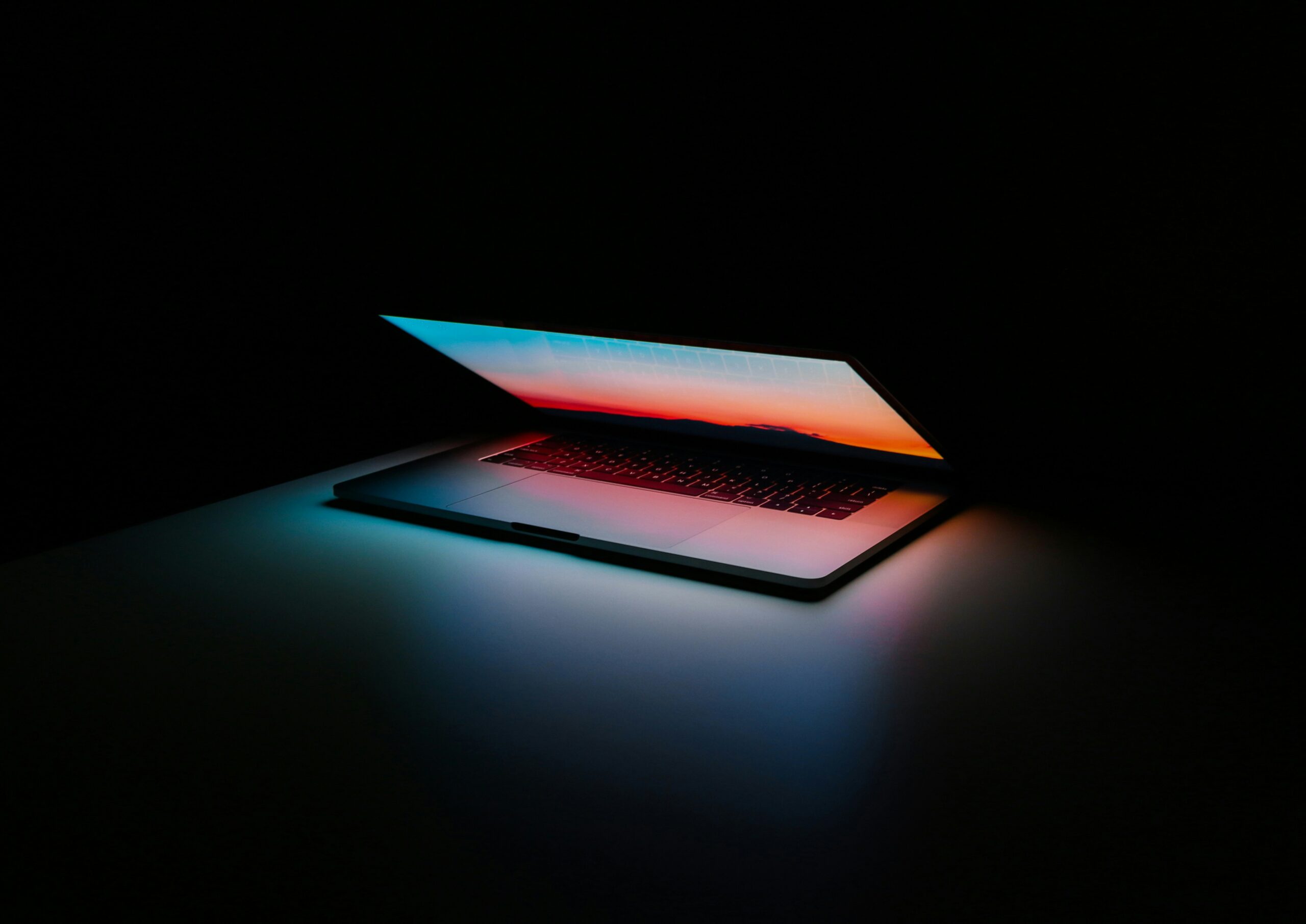 a laptop half open in a dark room on top of a table